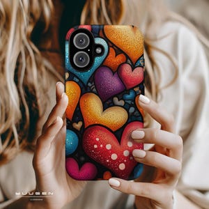 Op de afbeelding: Een kleurrijke telefoonhoes met een patroon van harten in rood, oranje, geel, blauw en paars. De hoes heeft een glanzende afwerking en een camera-uitsparing. De merknaam "YUUGEN CASES" staat onderaan.