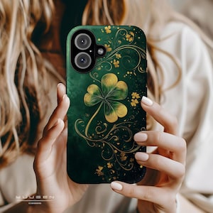 Op de afbeelding: Een groene en gouden telefoonhoes met een klavertje vier ontwerp. De klaver is goud met groene accenten en is omringd door gouden swirls.