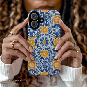 Op de afbeelding: Een telefoonhoesje met een blauw, wit en oranje tegelpatroon. Het ontwerp bevat bloemen- en citrusfruitmotieven. De hoes wordt vastgehouden door de handen van een persoon en de merknaam "YUUGEN CASES" is onderaan zichtbaar.