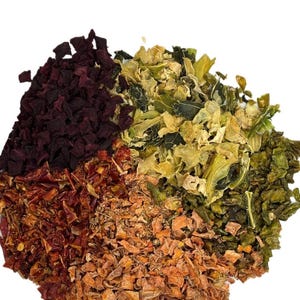 Puede incluir: Primer plano de un mont&oacute;n de verduras secas, que incluyen remolacha roja oscura, col rizada verde, zanahorias naranjas y pimientos rojos. Las verduras est&aacute;n dispuestas en un patr&oacute;n circular sobre un fondo blanco.