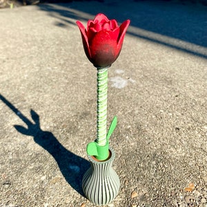 May include: A red tulip with a green stem and leaves in a gray striped vase.