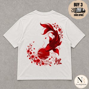 Può includere: Una t-shirt bianco sporco con una grande grafica rossa sul retro. Il design raffigura un pesce koi dettagliato che nuota sopra un sole rosso, circondato da rami di ciliegio in fiore e dal carattere kanji giapponese per koi in inchiostro rosso.