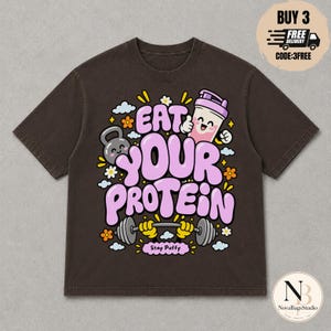 Könnte beinhalten: Ein dunkelbraunes T-Shirt mit kurzen Ärmeln und einem Grafikdruck mit dem Text EAT YOUR PROTEIN und Stay Puffy. Das Design zeigt eine lächelnde Kettlebell, einen Protein-Shaker und eine Hantel mit gelben Armen, umgeben von kleinen Blumen und Wolken.