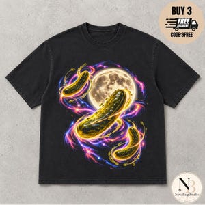 Könnte beinhalten: Ein schwarzes Kurzarm-T-Shirt mit einem Grafikdruck von drei leuchtend grünen Gewürzgurken, umgeben von wirbelnden violetten und blauen kosmischen Energiestrahlen und einem großen, detaillierten Vollmond in der Mitte des Designs auf der Vorderseite.