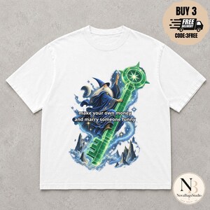 Könnte beinhalten: Ein weißes T-Shirt mit einer Grafik eines Zauberers in einer blauen Robe, der einen großen, leuchtend grünen Schlüssel hält. Der Text "make your own money and marry someone funny" ist in schwarzen Buchstaben über dem Zauberer und Schlüssel gedruckt.