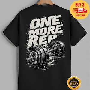 Könnte beinhalten: Ein schwarzes Kurzarm-T-Shirt mit einem Grafikdruck auf der Rückseite. Das Design zeigt den weißen, abgenutzten Schriftzug ONE MORE REP über einer detaillierten Illustration einer schwarzen Hantel mit Gewichten. Die Hantel trägt den Text CERFELT ZEPET.