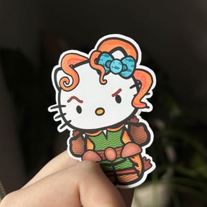 May include: A sticker depicting a cartoon cat character with orange hair and a blue bow. The cat is dressed in a green and brown outfit with orange details. The cat has an angry expression.