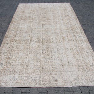May include: A rectangular area rug featuring a faded, distressed pattern in shades of beige, cream, and light brown. The rug has a low-pile texture with a visible, worn-in appearance across its entire surface, displaying intricate, muted floral motifs.