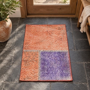 May include: A rectangular area rug featuring a patchwork design with a large orange section at the top and two smaller bottom panels in orange and purple. The sections are joined by a visible white stitched seam, creating a textured appearance.