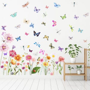 May include: A wall decal featuring a vibrant garden scene with colorful flowers, butterflies, and dragonflies. The design includes pink, yellow, and white flowers, with various butterflies and dragonflies in shades of blue, pink, and green. The decal is designed to be applied to a wall.