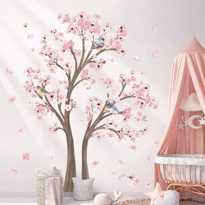 May include: A wall decal featuring a blossoming cherry tree with pink flowers and brown branches. Three blue and yellow birds perch on the branches. Pink flower petals are scattered around the tree. A pink canopy and crib are in the background.