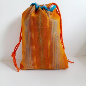 Peut inclure: Sac à cordon orange avec une bordure rayée bleu et blanc. Le sac est fait d'un tissu tissé et a un long cordon orange.