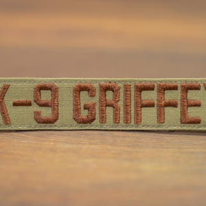 Puede incluir: Un parche de tela beige con texto bordado en marrón que dice "K-9 GRIFFEY".