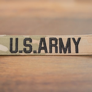 Może przedstawiać: Naszywka z tkaniny w kolorze beżowym i zielonym w kamuflażu z czarnym haftem z napisem "U.S. ARMY".