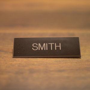 May include: A black rectangular table card with the name "SMITH" printed in white.