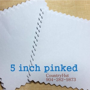 May include: A stack of white 5 inch square fabric squares with pinked edges. The fabric is smooth and has a slight sheen. The squares are stacked on top of each other, with the top square slightly offset from the bottom square. The text "5 inch pinked" is printed in blue on the top square. The text "CountryHut 904-282-9873" is printed in brown on the bottom square.