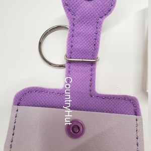 May include: A lavender fabric key chain with a small pocket and a snap closure. The key chain has a metal ring and the text "CountryHut" is printed on the fabric.