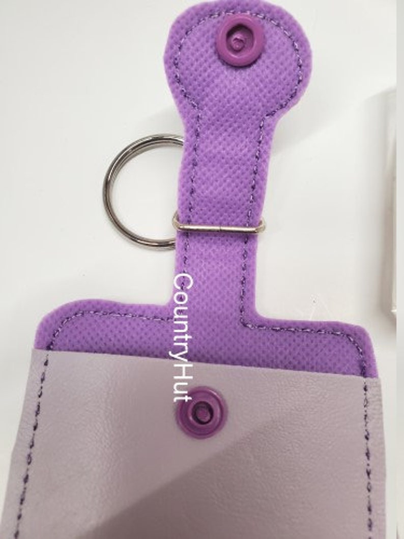 May include: A lavender fabric key chain with a small pocket and a snap closure. The key chain has a metal ring and the text "CountryHut" is printed on the fabric.