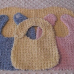 Könnte beinhalten: Drei Baby-Lätzchen in verschiedenen Farben: blau, gelb und rosa. Die Lätzchen sind aus weichem, flauschigem Material und haben einen Klettverschluss.