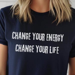 Könnte beinhalten: Marineblaues T-Shirt mit dem weißen Text "CHANGE YOUR ENERGY CHANGE YOUR LIFE". Das Shirt hat einen Rundhalsausschnitt und hochgekrempelte Ärmel. Das Wort "NAVY" befindet sich in einem marineblauen Kreis.