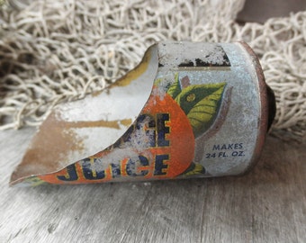 May include: A vintage, dented, orange juice can with a faded orange and green label. The label reads "Orange Juice" and "Makes 24 Fl. Oz."