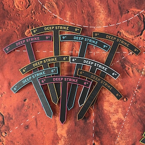 May include: Several black game pieces, each labelled "DEEP STRIKE" and marked with 6" and 9" measurements. The pieces, in various colours, are arranged on a reddish-brown game board with a map design.