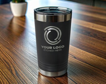 Pode incluir: Um copo de aço inoxidável preto fosco com tampa de plástico transparente. A frente apresenta um logotipo circular prateado acima do texto "YOUR LOGO ETCHED HERE" em uma fonte sem serifa. O copo tem um formato cilíndrico cônico.