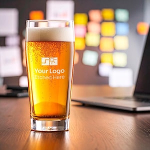 以下が含まれることがあります： 黄金色の液体と厚い白い泡が入った透明なパイントビールグラス。グラスの前面中央には、星のアイコンとYour Logo Etched Hereというテキストが白くプリントされており、ロゴデザインが施されています。