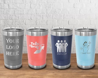 Könnte beinhalten: Vier Edelstahlbecher mit Deckel. Die Becher sind grau, korallenrot, marineblau und hellblau. Jeder Becher hat ein anderes Design: "YOUR LOGO HERE", "Team Bride", eine Gruppe von Figuren und "I Said Yes!".