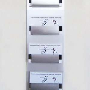 May include: Four white cards with a floral design and the text "CONTEMPORARY ELEMENTS FOR THE HOME AND OFFICE" and "PATRICIA LINKEY" are displayed on a white wall.