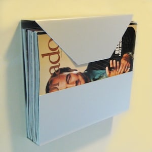 May include: A light blue metal magazine holder with a stack of magazines inside. The top magazine has a picture of a man on the cover with the word "Playboy" visible.