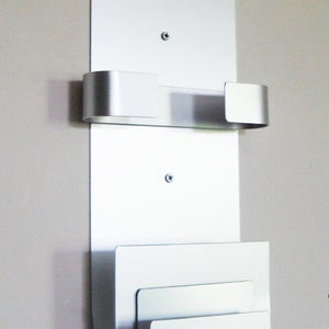 May include: Silver wall mounted mail holder with three slots. The slots are curved and have rounded edges.