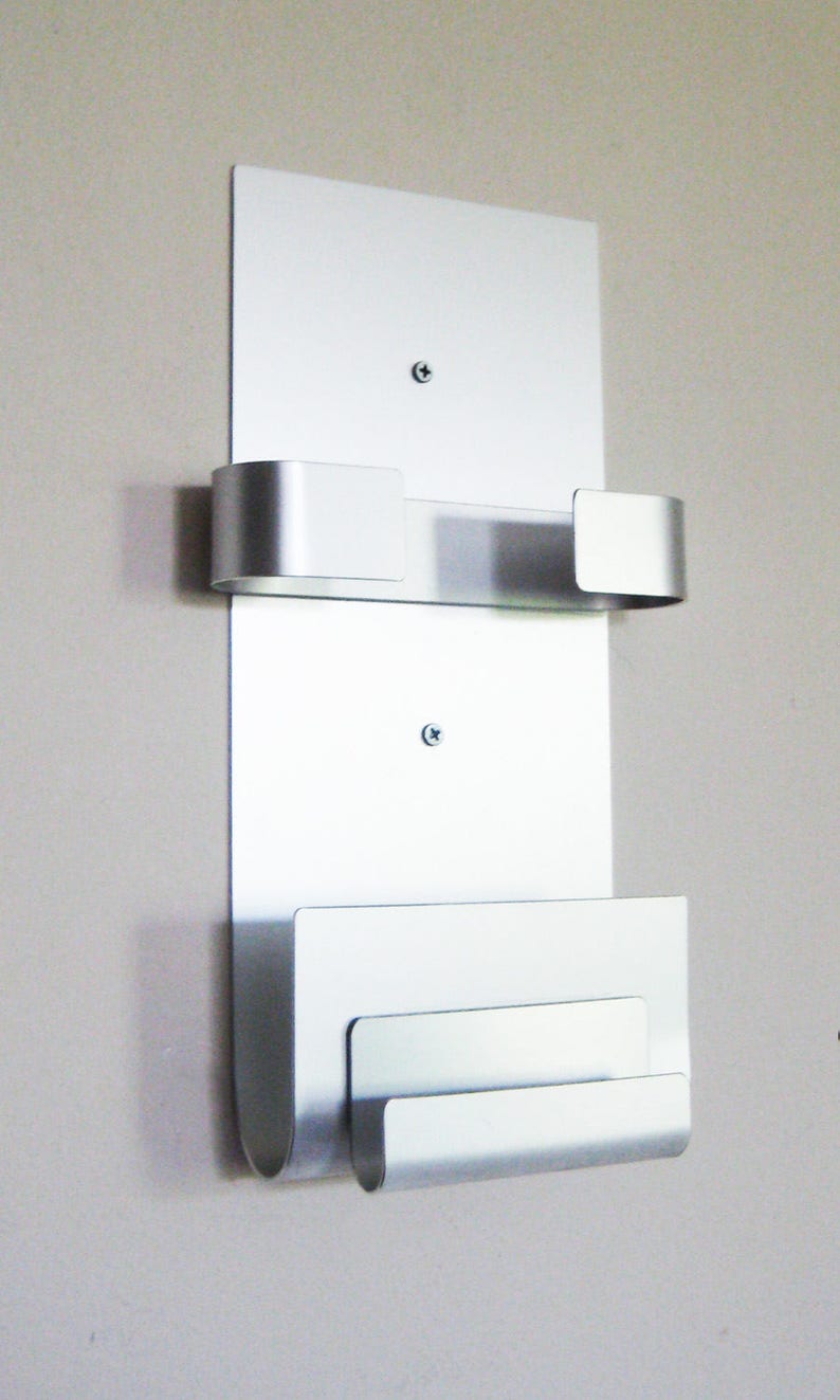 May include: Silver wall mounted mail holder with three slots. The slots are curved and have rounded edges.