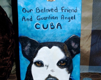 May include: A blue wooden box with a gold latch, painted with a black and white dog portrait and the words "Our Beloved Friend And Guardian Angel CUBA August 2000 - July 4, 2012".
