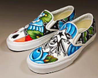 Puede incluir: Zapatillas Vans slip-on pintadas a mano con un diseño colorido que presenta personajes de la película "Pesadilla antes de Navidad". Las zapatillas tienen un fondo blanco con detalles azules, verdes, naranjas y negros.