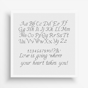 May include: A square white fabric piece featuring black embroidered text. The design includes the full alphabet in uppercase and lowercase letters, numbers 0-9, punctuation, and the phrase "Love is going where your heart takes you!" in a script font.