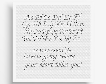 May include: A square white fabric piece featuring black embroidered text. The design includes the full alphabet in uppercase and lowercase letters, numbers 0-9, punctuation, and the phrase "Love is going where your heart takes you!" in a script font.