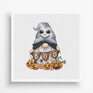 May include: A gray and white gnome with a stitched-on skull face holds a banner that reads "BOO" in orange and black letters. The gnome is surrounded by orange pumpkins and candy canes.