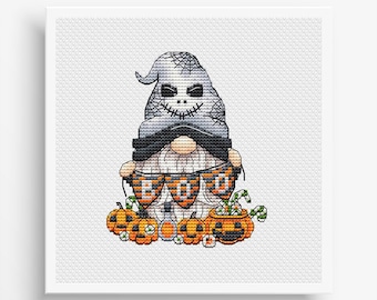 Op de afbeelding: Een grijze en witte gnome met een gestikt schedelgezicht houdt een spandoek vast met de tekst "BOO" in oranje en zwarte letters. De gnome wordt omringd door oranje pompoenen en snoepstokken.