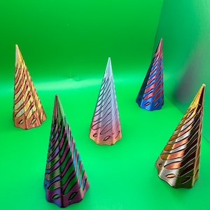 May include: Five decorative, iridescent, cone-shaped ornaments with a swirling pattern. The ornaments are made of a shiny, metallic material and are arranged on a green surface.