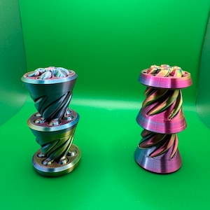 May include: Two 3D printed, iridescent, multi-colored, stacked, cone-shaped objects. The objects are made of plastic and have a swirling pattern.