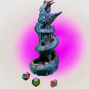 May include: A detailed, blue and green serpent-shaped dice tower with an open mouth design. The tower has a castle-like structure in the middle. Three multi-sided dice in shades of red, green, and gold are at the base. The background has a pink gradient.
