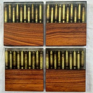 May include: Four square wooden coasters with a clear epoxy resin top. Each coaster features a grid of gold-colored bullet casings.