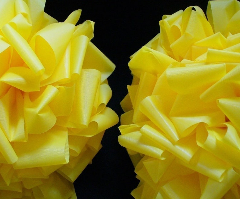 May include: Two large yellow fabric bows, made of multiple layers of ribbon, are arranged side by side against a black background.