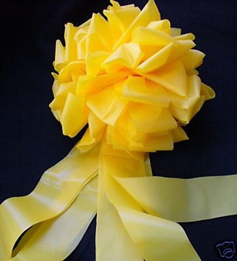 May include: A large yellow satin bow with long tails. The bow is made of multiple layers of fabric and has a fluffy, voluminous appearance.
