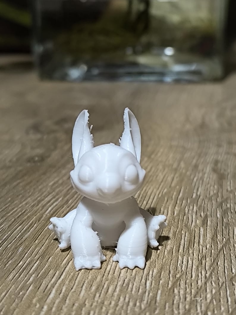 May include: White 3D printed figurine of a cartoon character with large ears and a wide smile. The character is sitting with its legs crossed and its arms resting on its knees.