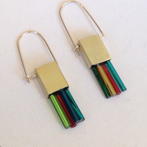 May include: A pair of gold-toned earrings with a rectangular gold top and a colorful fringe of red, green, and blue-green beads. The earrings have a simple, curved hook design.