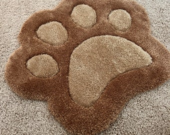 以下が含まれることがあります： 隆起したデザインの茶色のふわふわの足跡の敷物。敷物は柔らかくふわふわした素材で作られており、薄い茶色です。