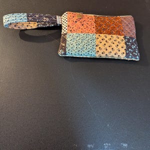 May include: A small quilted patchwork purse with a brown, blue, and orange color scheme. The purse has a single handle and a zipper closure.