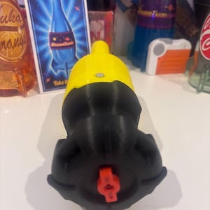 May include: A yellow and black bottle stopper with a red valve. The stopper is in front of a sign that says "Nuka-Cola Quantum" with a blue bottle design. Other bottles are in the background.